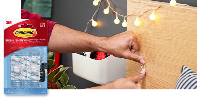 Command™ Mini Hooks, behins the product in package, a man is placing a mini hook on a headboard to hang string lights on.
