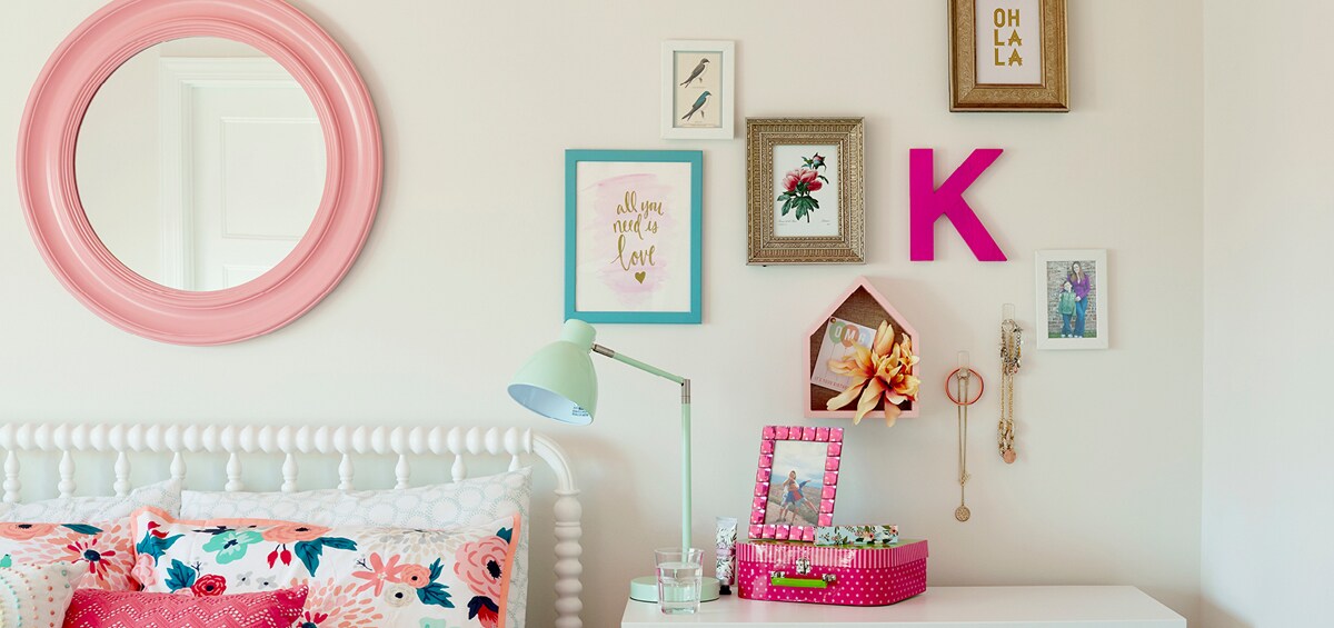 Une chambre à coucher de différentes teintes de roses et de bleus clairs, du couvre-lit aux décorations murales.