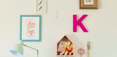 Un mur de chambre à coucher blanc auquel sont suspendues des photos encadrées de différentes tailles et quelques lettres.
