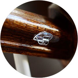 Closeup of a clear cord clip secured to a wood staircase railing.
