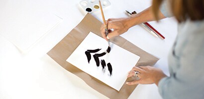Woman painting an abstract Christmas tree using black paint.
