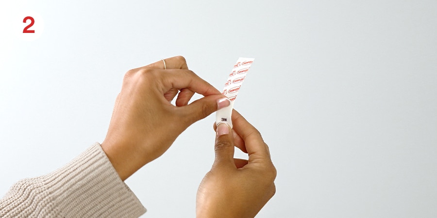 Hands remove the red iner from the adhesive strip.