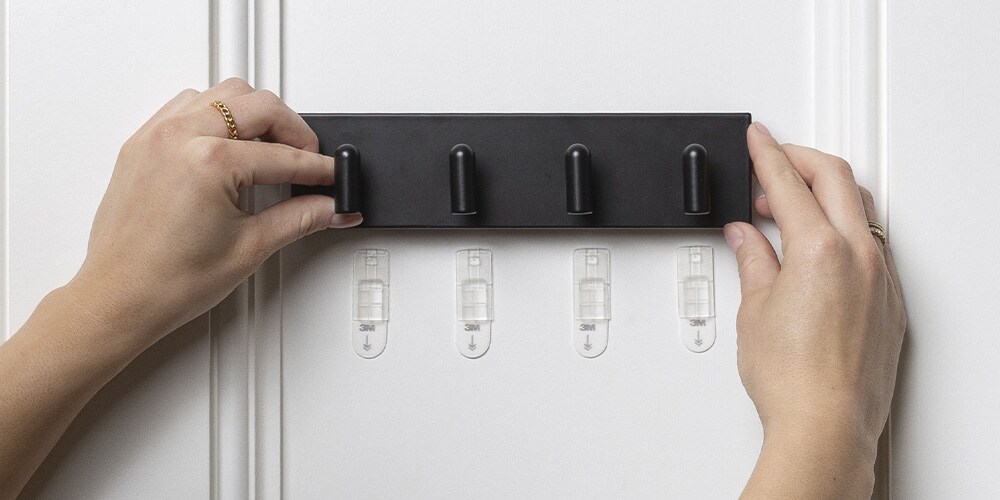 Command™ Metal Key rail being placed on a wall showing damage-free backings.
