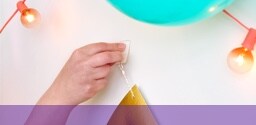 A hand sticking an adjustable adhesive hook to a wall with string lighting and decorations.