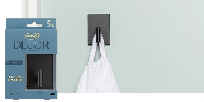Command™ Large Metal Towel hook in matte black holding a white towel on a mint green wall.
