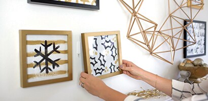 Une femme accrochant au mur des images peintes à la main dans des cadres dorés.
