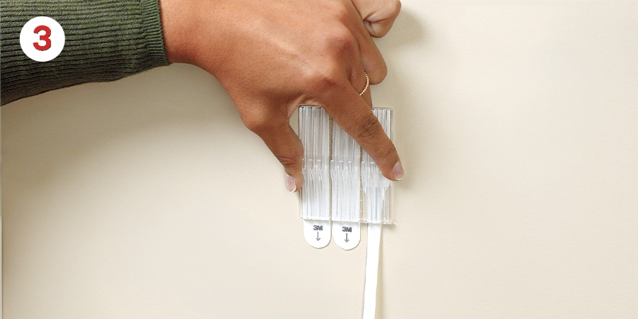 Hands pull the strips down against the wall to remove.