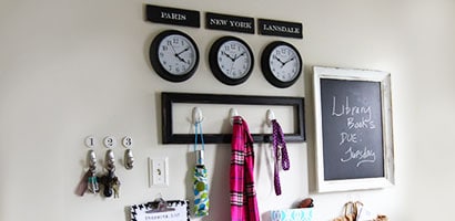 The finished results of an organized mudroom with wall hooks for keys, clothing and lists along with three wall clocks displaying the time in different cities.
