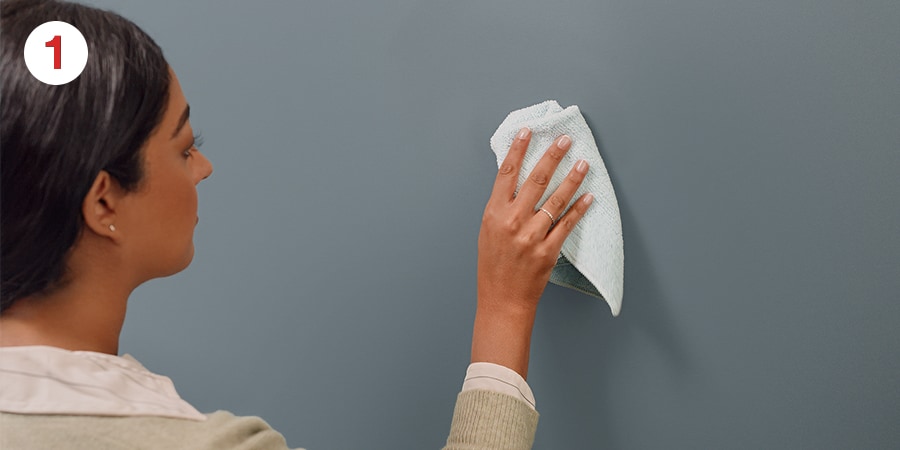 Person wiping a gray wall with a light blue cloth.
