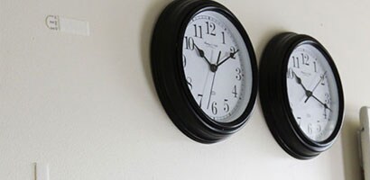 Deux horloges murales ovales avec des bordures noires et des visages blancs accrochées sur un mur.
