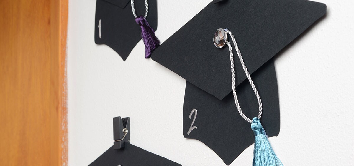 3 cutout graduation hats hanging on Command Slate Spring Clips.
