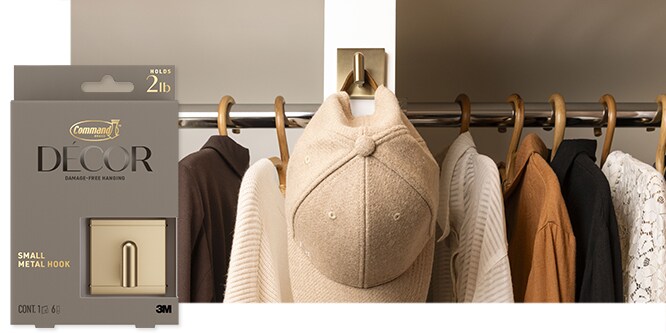 Command™ Small Metal Hook in brushed brass holding a hat on a wall in a closet.
