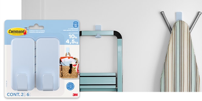 Command™ X-Large Hooks on a wall holding a step ladder, and an ironing board.
