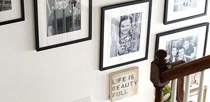 View from top of staircase looking down at the wall populated with hanging pictures. 
