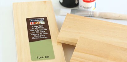 Trois planches de pin clair posées sur une table à côté d’un petit pinceau.
