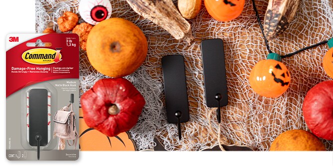 Command™ Medium Black Metal Hooks on a table with halloween decorations surrounding them. Product in package in lower left corner.
