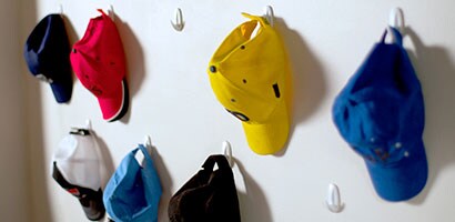 Several colored baseball caps hanging from Command Designer Medium Hooks.
