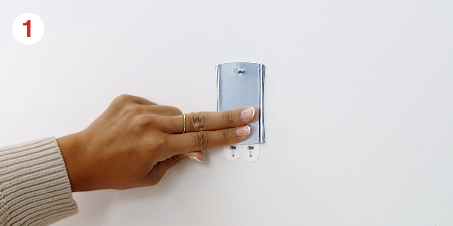 A hand gently holding the hanger in place against the wall.