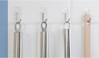 Metal kitchen utensils hung on a wall using clear Command™ Hooks.
