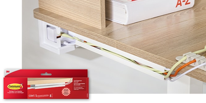 Command™ Cord Organizer Channel securing three cords along the underside of a desk. Product in package in lower left corner.
