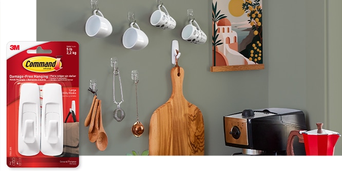 Command™ Large Utility Hook, behind the product in package, the hook is used to hold a cutting board on a wall next to measuring spoons, and mugs.
