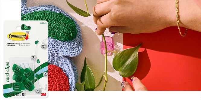 Command™ Cord Clips on a wall holding up a vine. Packaging shown on the left.
