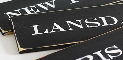 Trois planches de pin peintes en noir portant les noms de ville transférés peints en blanc.
