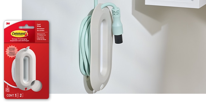 Command™ Cord Wrap holding a wrapped light blue cord against a white wall. Product in package in lower left corner.
