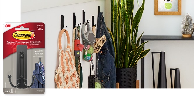 Command™ Large Double Hook, behind the product in package, hooks are used to hold various bags and pet supplies on a wall.
