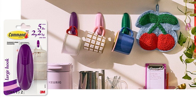 Command™ Large Designer Hook  holding colorful mugs and a cherry potholder, next to a pink coffee maker and clipboard. Package shown on the left.
