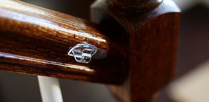 Gros plan d’une Pince pour cordon transparente fixée sur le côté d’une rampe d’escalier en bois.
