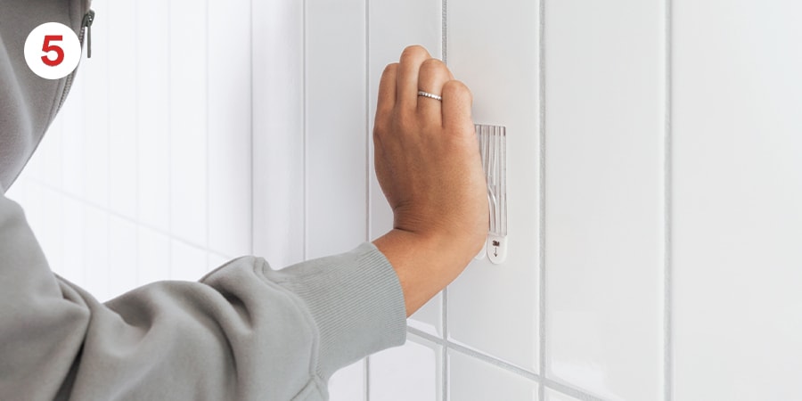 Step 5 - To ensure adhesive hold, hands show the base being firmly pressed to the wall.