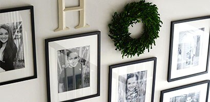 View from top of staircase looking down at the wall populated with hanging pictures and green topiary wreath. 
